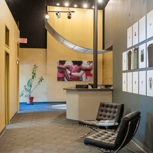 Interior of a modern waiting area with chairs, a reception desk, and workout images.