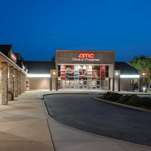 A modern office breakroom with a large table, chairs, and a small kitchen area.