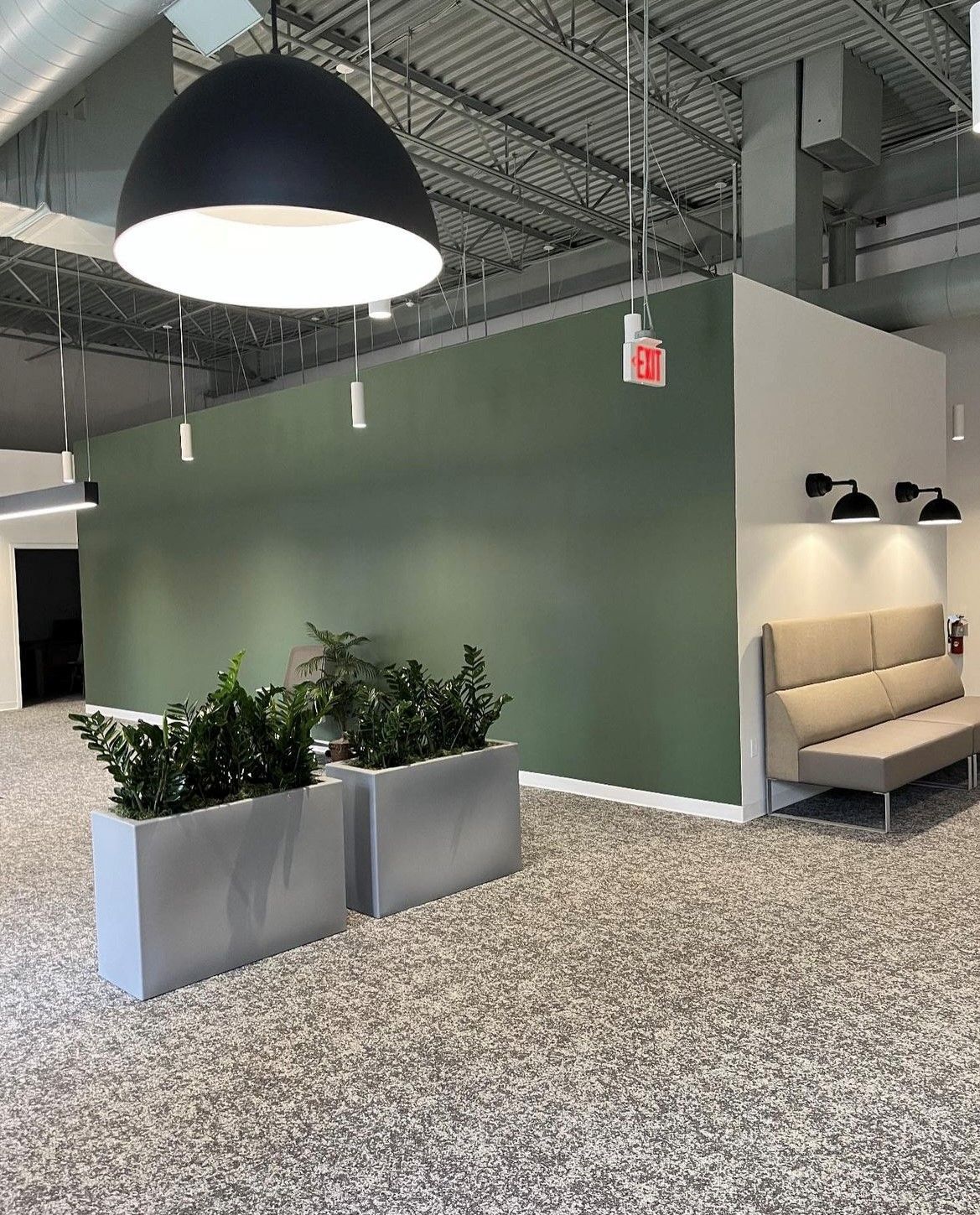 Modern office interior with green wall, plants, seating area, and terrazzo flooring.