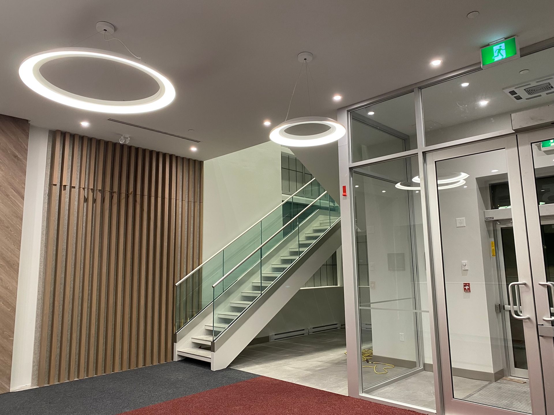 Lobby with stairs, glass doors, and decorative circular lights. Wood panel wall on the left, red and blue floor.