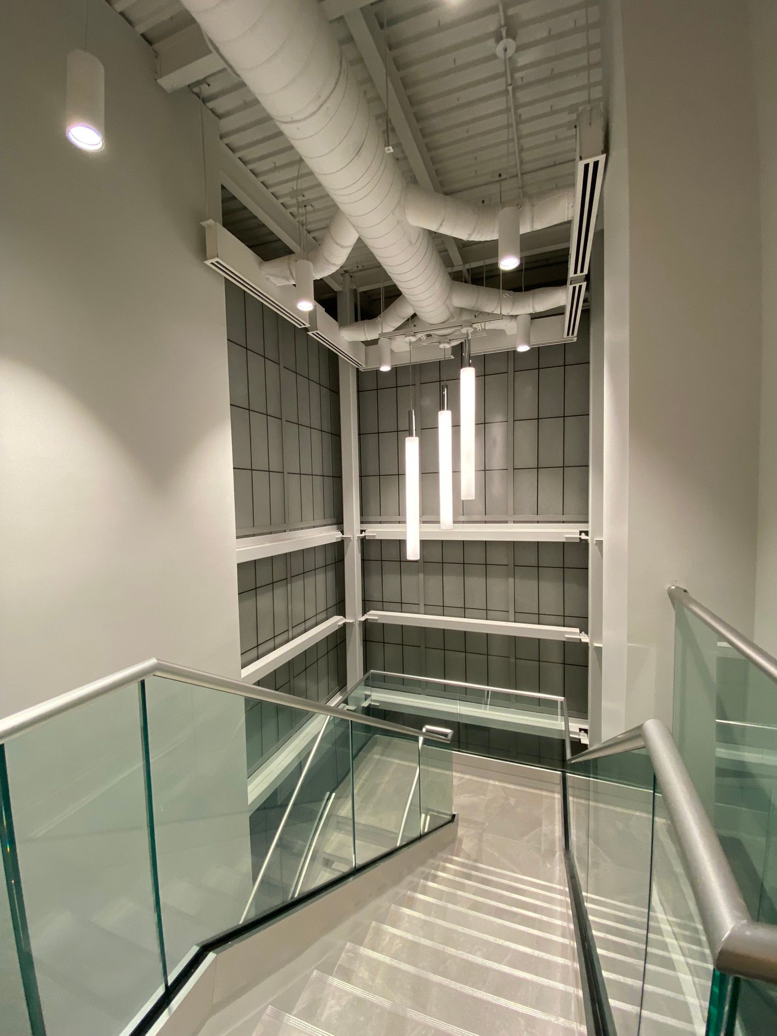 Stairwell with glass railings and modern lighting; white walls and geometric paneling.
