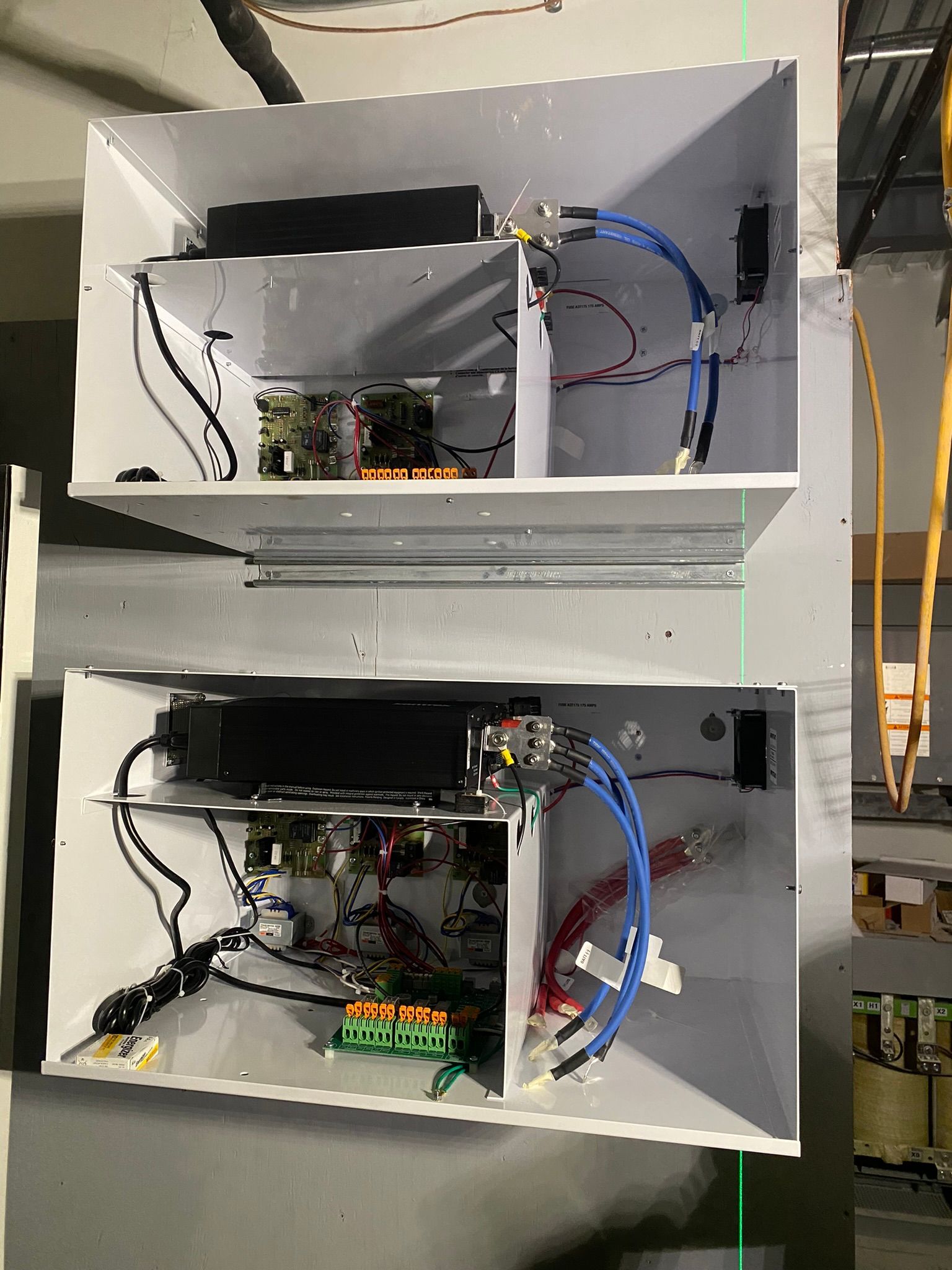 Two open gray electrical boxes mounted on a wall, revealing circuit boards, wires, and other components.