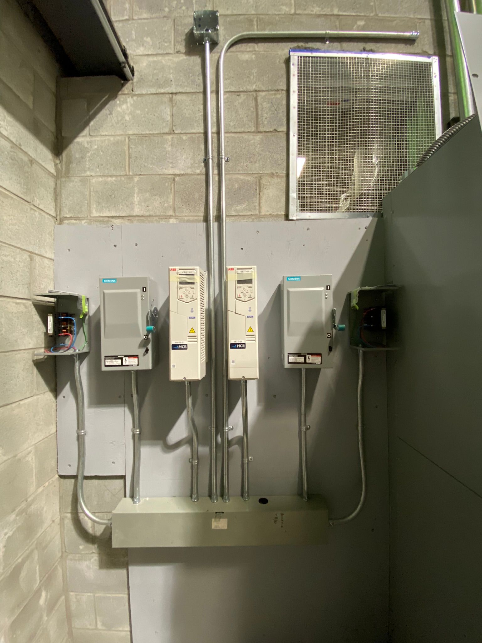 Electrical control panel with three inverters and conduit on a gray wall.