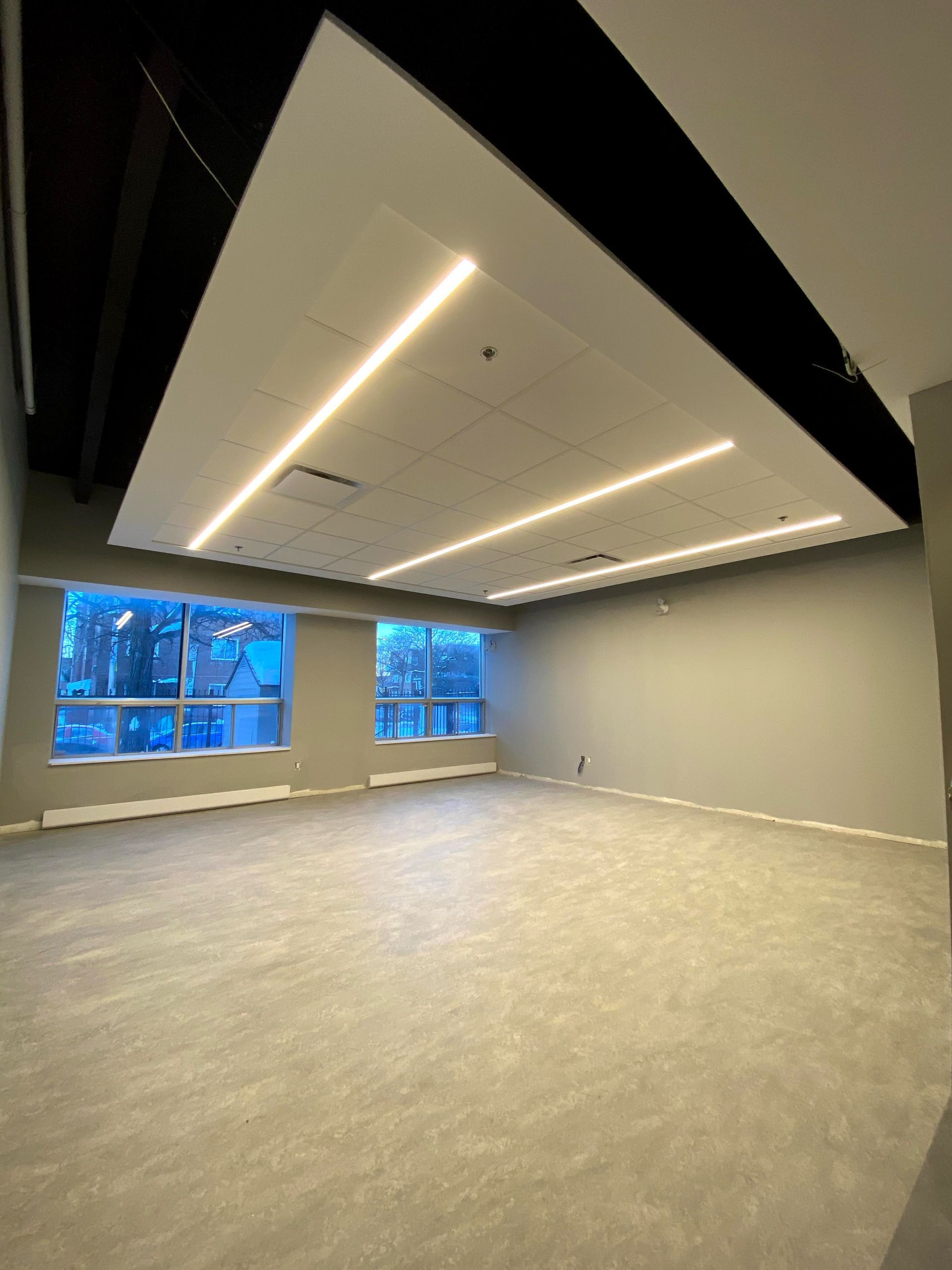 Empty room with large windows, gray walls, carpet, and ceiling lights.