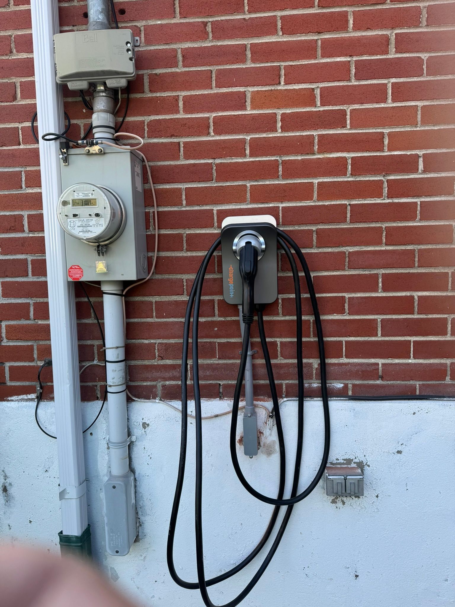 Electric vehicle charger mounted on a brick wall, next to a utility meter.