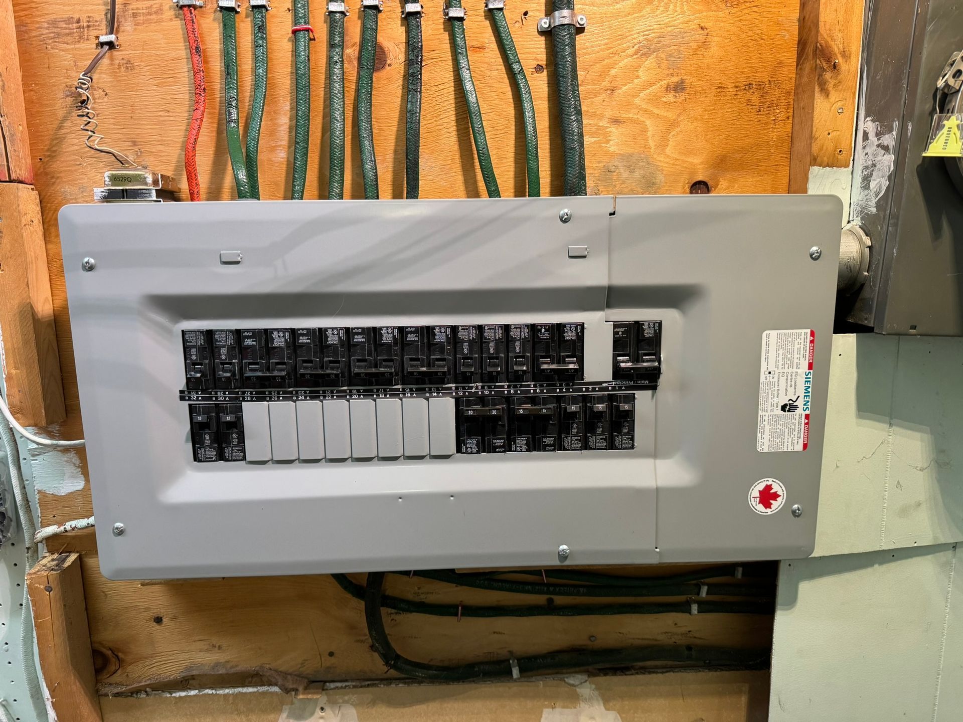 Electrical panel mounted on a wood wall, with multiple circuit breakers and wires.