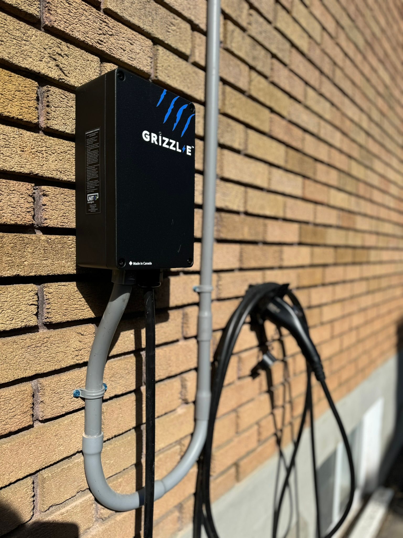 Black Grizzl-E EV charger box mounted on brick wall with charging cable.