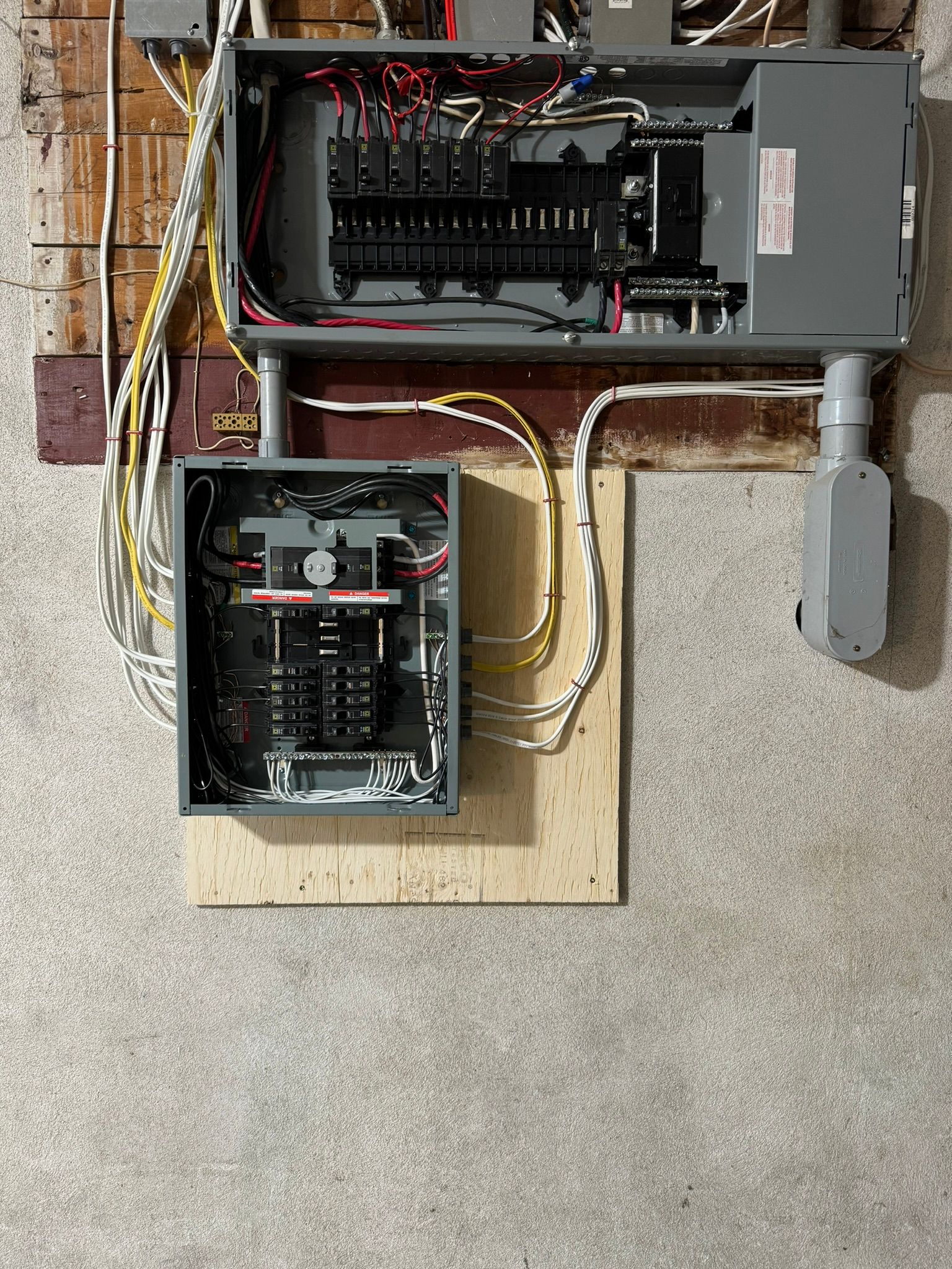 Electrical panels mounted on a wall. One is open with circuit breakers visible. Wires and conduits connect the panels.