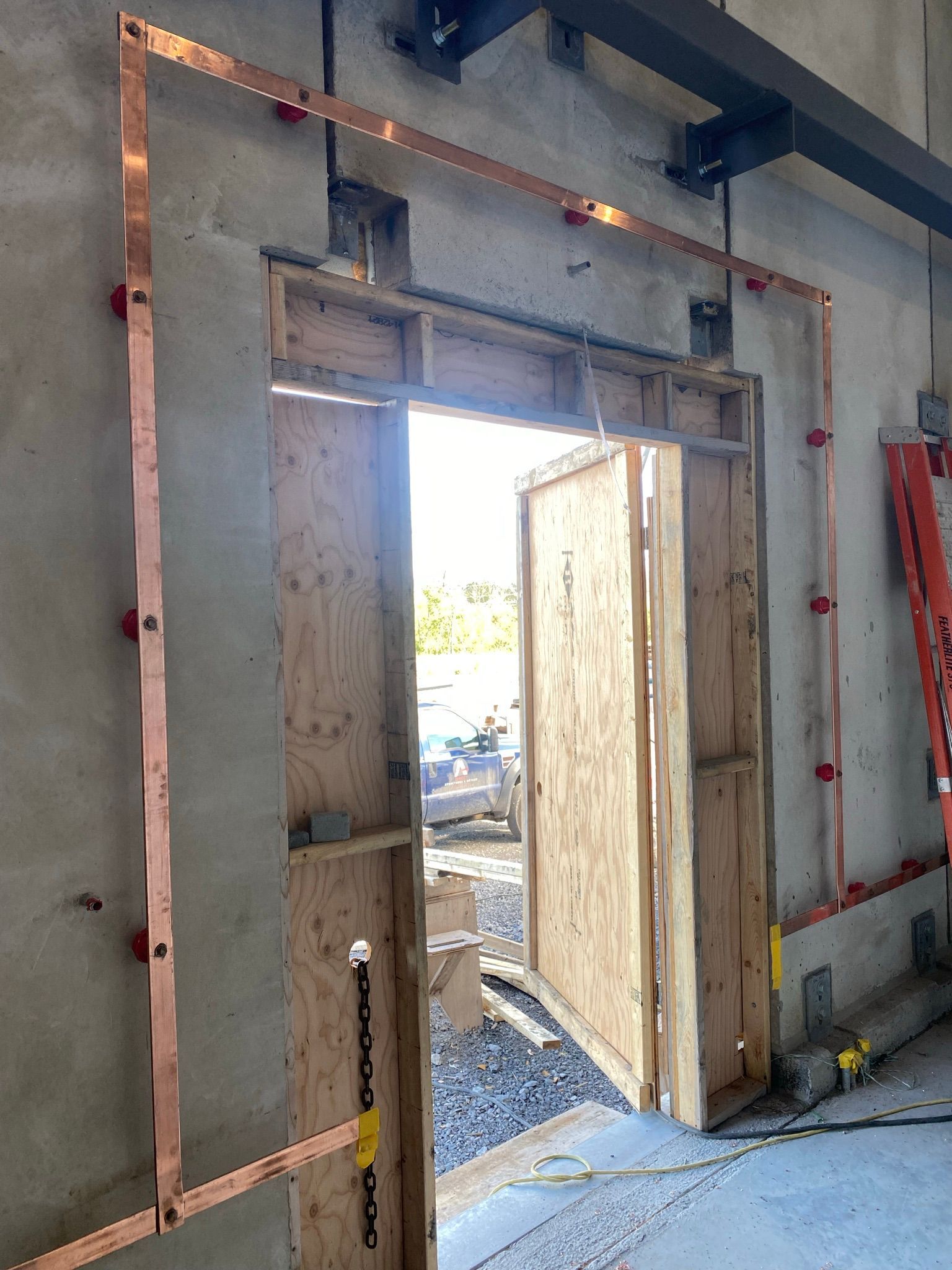 Copper strips outlining a doorway under construction, attached to concrete and wood with red fasteners.