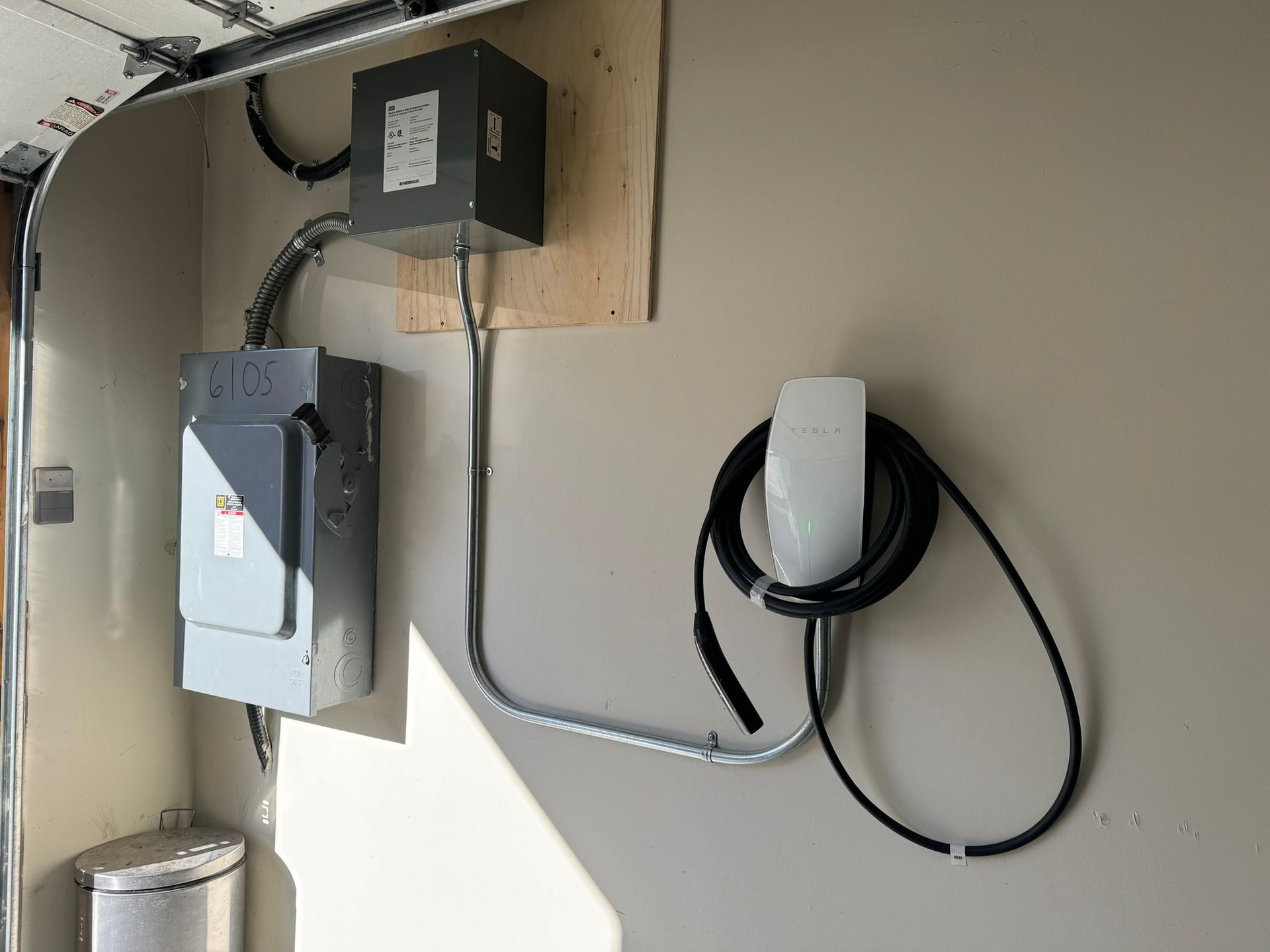 EV charger installation in a garage. Gray electrical box and charger mounted on a wall with black cable.