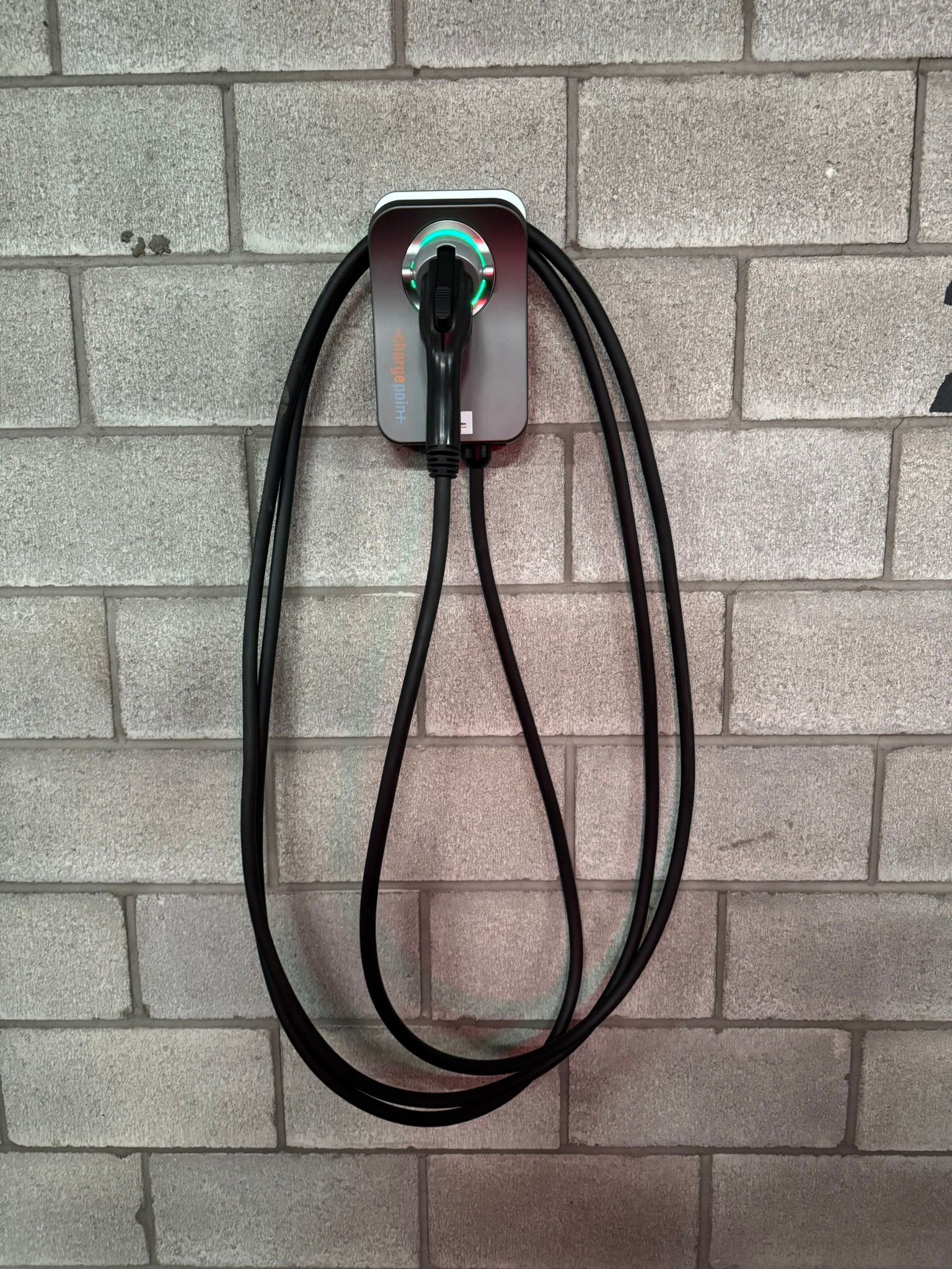 Electric vehicle charger mounted on a gray brick wall. Black cable hangs down.