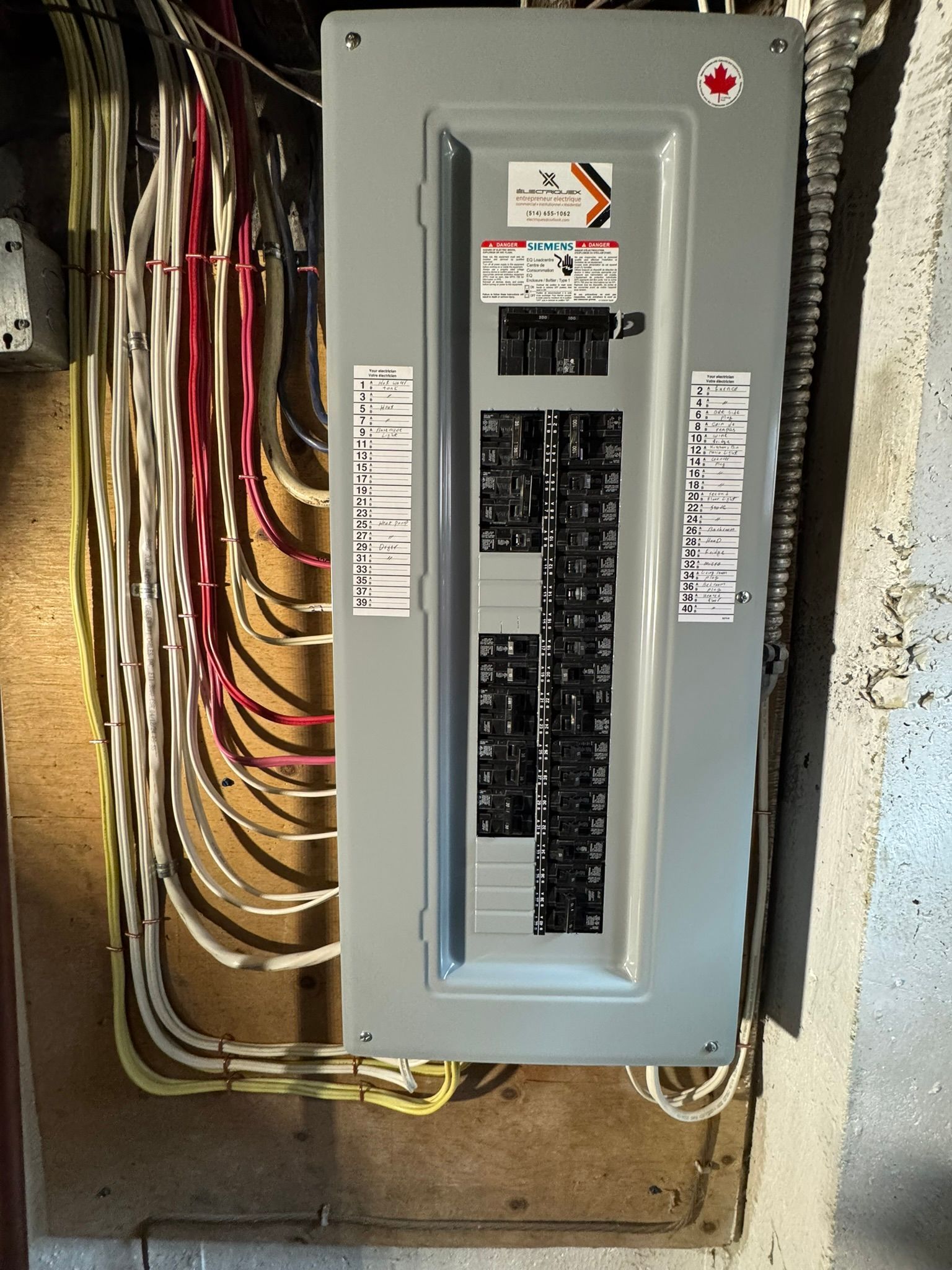 Electrical panel with circuit breakers and wires. Grey panel mounted on a wall.