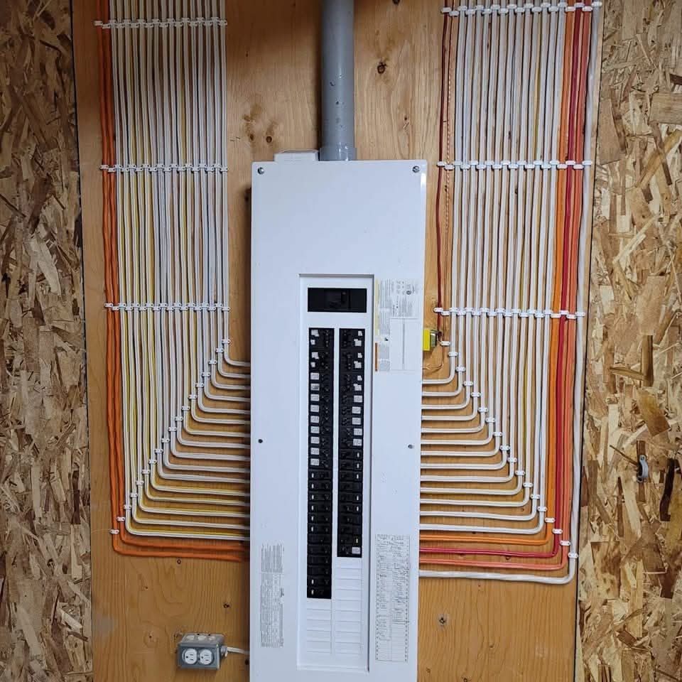 Electrical panel with organized wiring on a wooden wall, white panel, gray conduit, and organized wire runs.