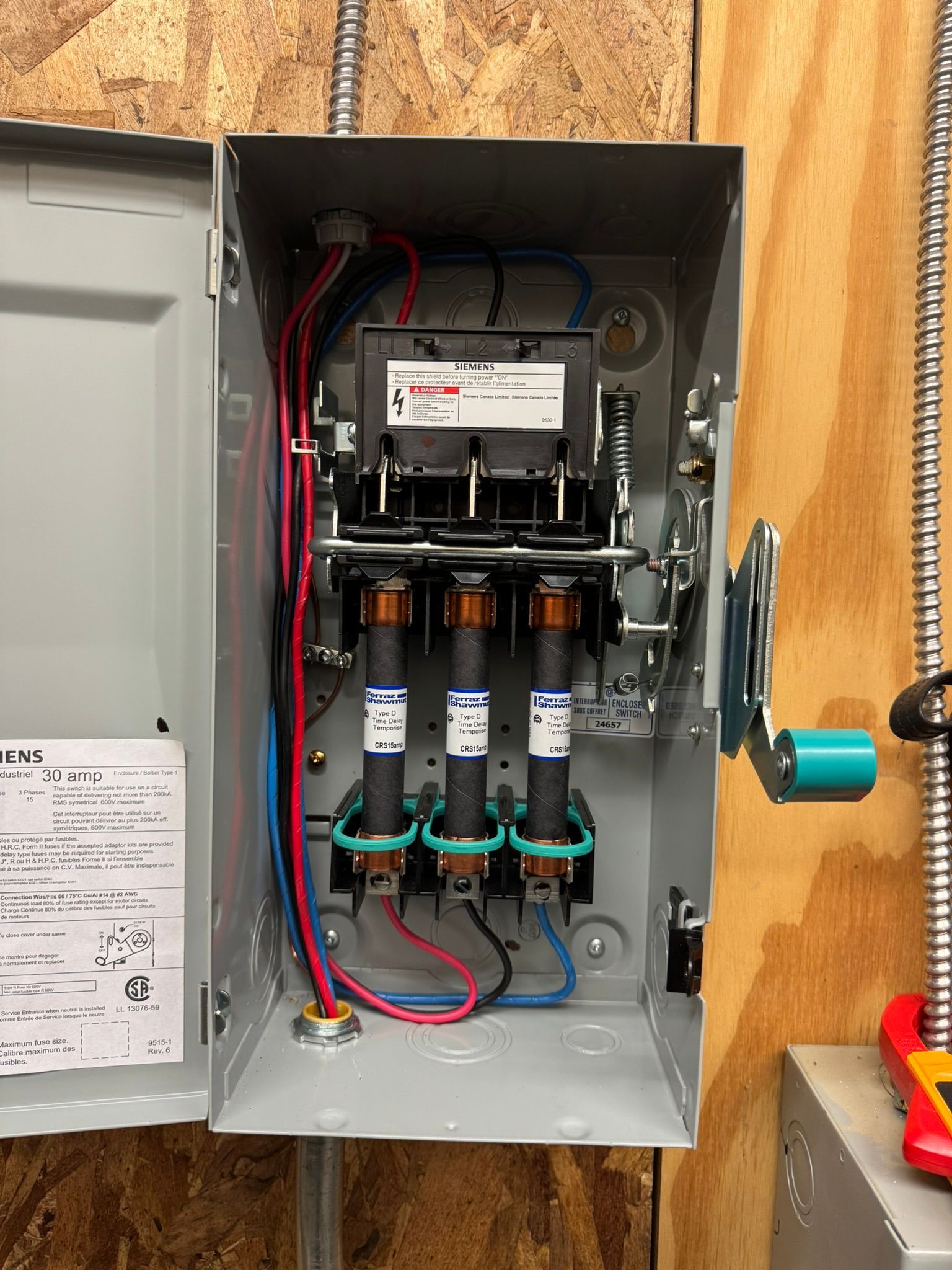 Open metal electrical switch box with three fuses, wires, and handle.