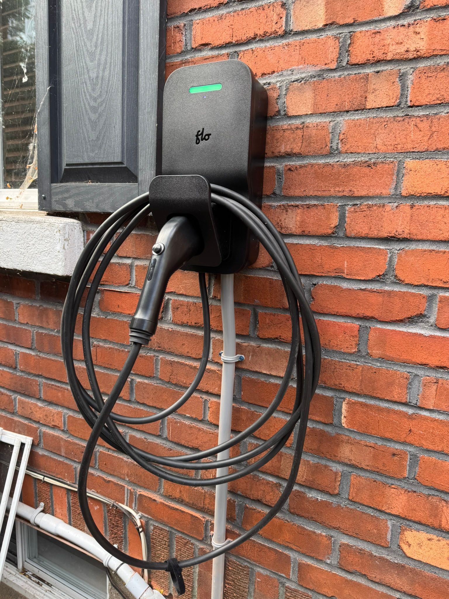 Black electric vehicle charger mounted on a brick wall with charging cable coiled.