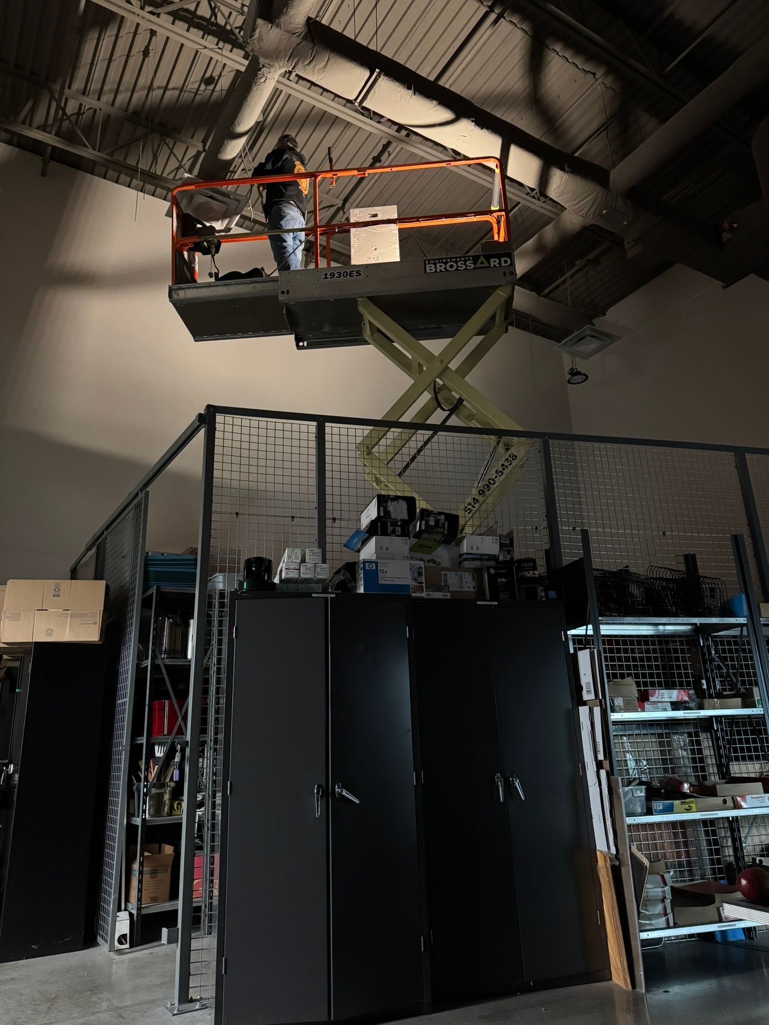 Person on scissor lift working on ceiling in industrial space.