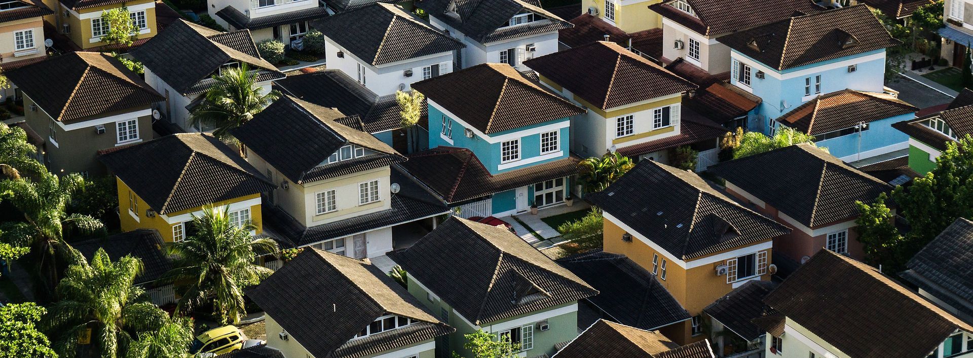 Aerial view of a neighborhood with colorful houses and dark roofs. Lush green trees surround the homes.