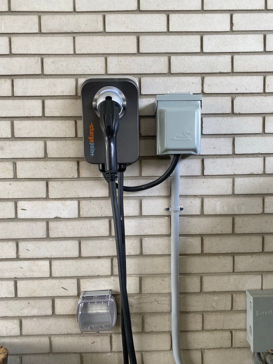 Electric vehicle charger and electrical box mounted on a brick wall.