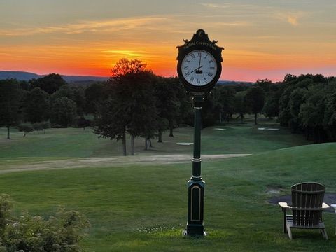 A clock stands in the middle of a golf course at sunset