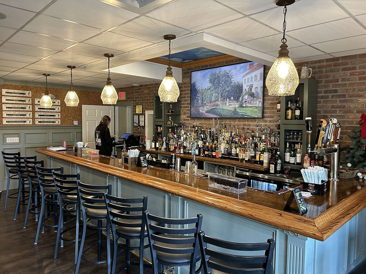 A restaurant with a long bar and stools and a television on the wall.