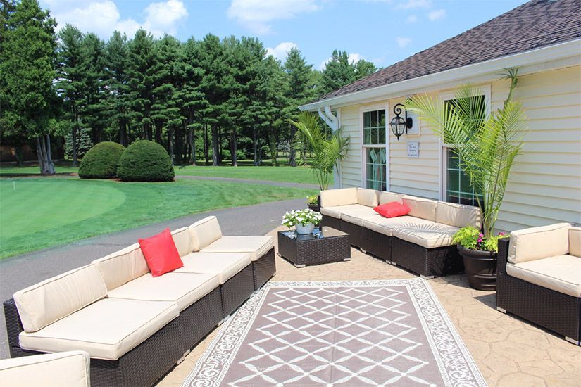A patio with a lot of furniture and a rug in front of a house.