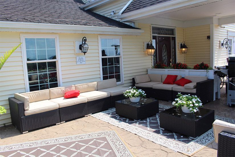 A patio with a couch , table , and rug in front of a house.