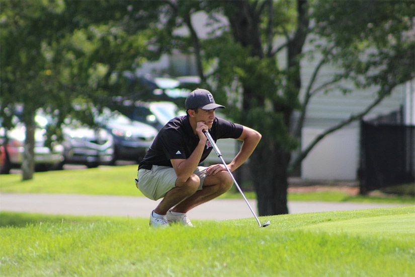 A man is squatting down while holding a golf club on a golf course.
