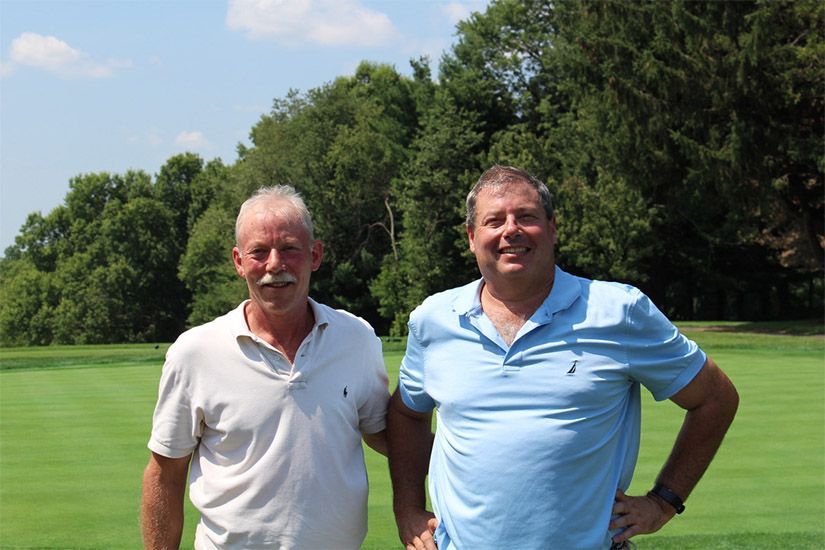Two men are standing next to each other on a golf course.