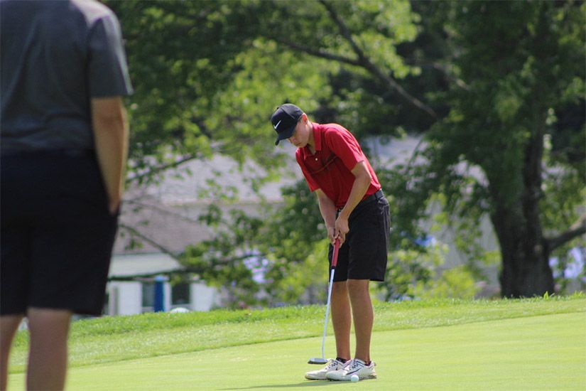 A man is putting a golf ball on a green while another man watches.