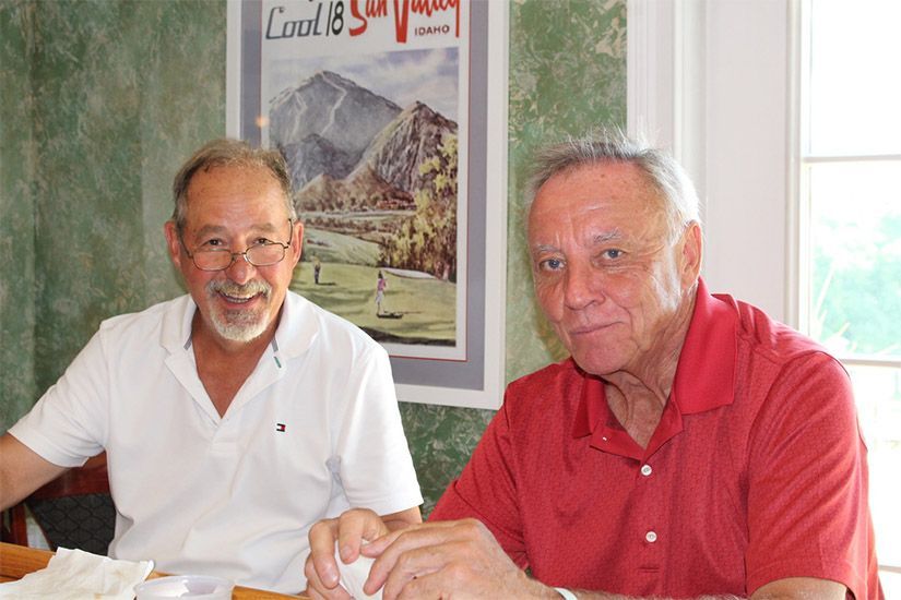Two men are sitting at a table in front of a poster that says louis & son