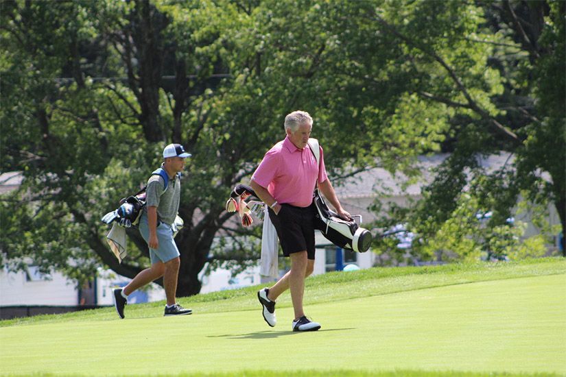 A man in a pink shirt is carrying a golf bag on a golf course.