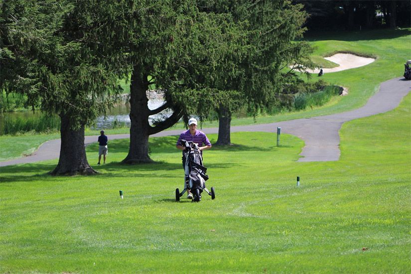 A man is pushing a golf cart on a golf course.
