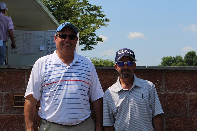 Two men standing next to each other with one wearing a titleist hat