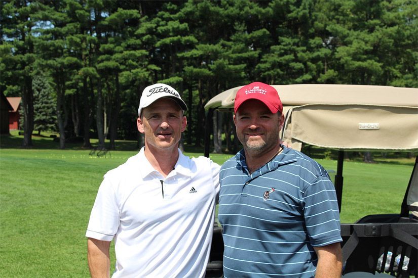 Two men are posing for a picture in front of a golf cart on a golf course.
