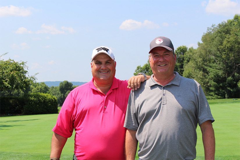 Two men are standing next to each other on a golf course.