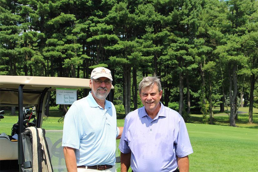 Two men are standing in front of a golf cart on a golf course.