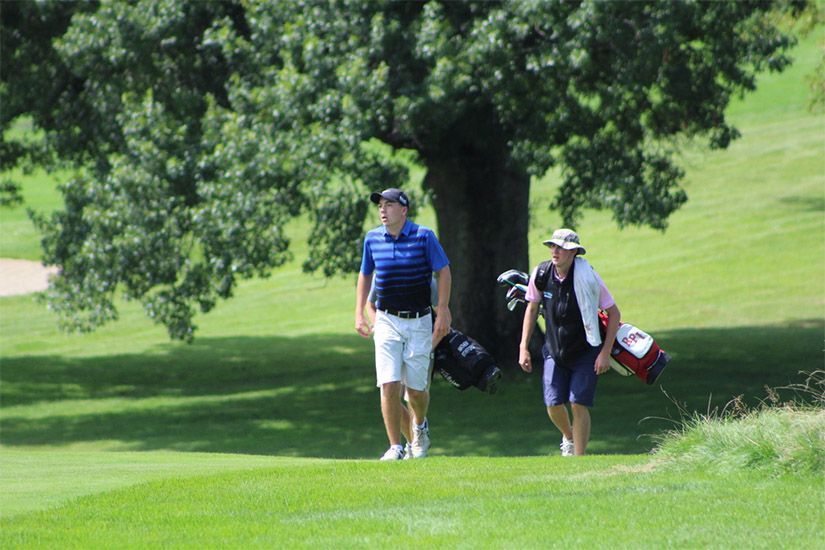 Two men are walking on a golf course carrying golf bags.