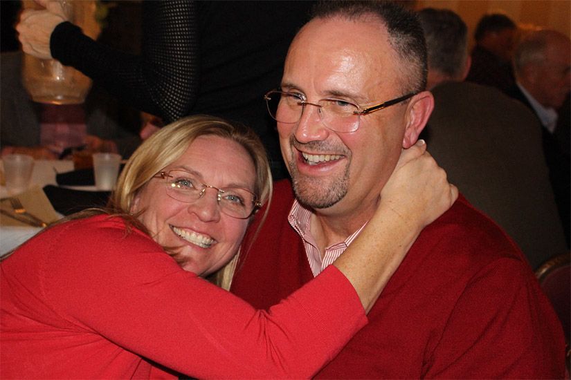 A man and a woman are hugging each other and smiling at the camera.