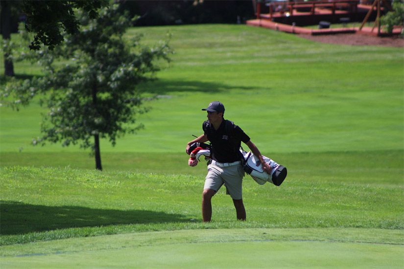 A man is carrying a golf bag on a golf course.