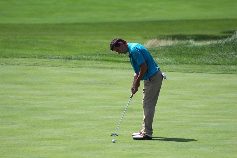 A man in a blue shirt is putting a golf ball on a green.