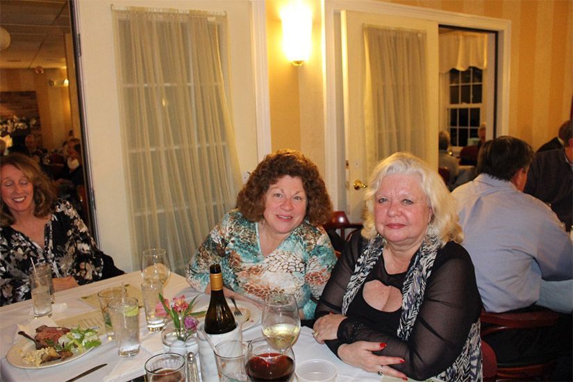 Two women are sitting at a table with a bottle of wine
