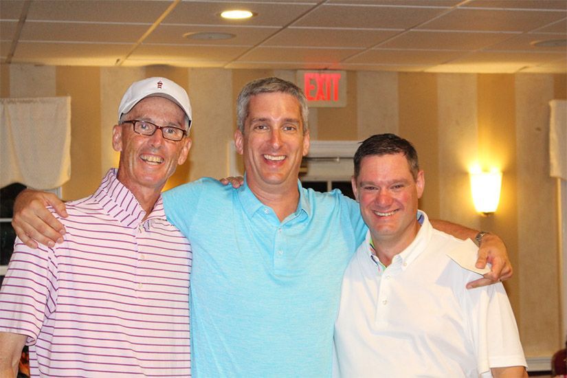 Three men are posing for a picture in a room with an exit sign in the background.