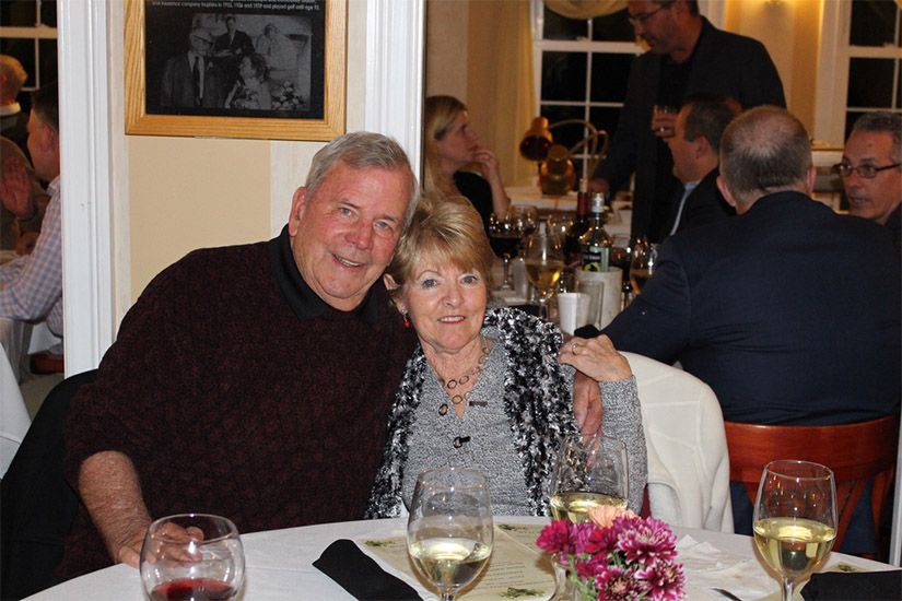 A man and woman are posing for a picture at a table with wine glasses