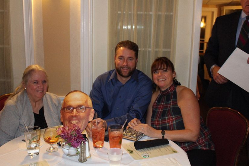 A group of people are sitting at a table with a man 's head on the table.