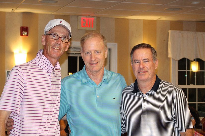 Three men are posing for a picture in a room with an exit sign in the background.