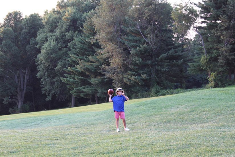 A young boy in a blue shirt is throwing a football in a field.