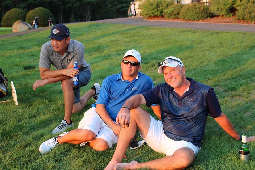 Three men are sitting on the grass on a golf course.