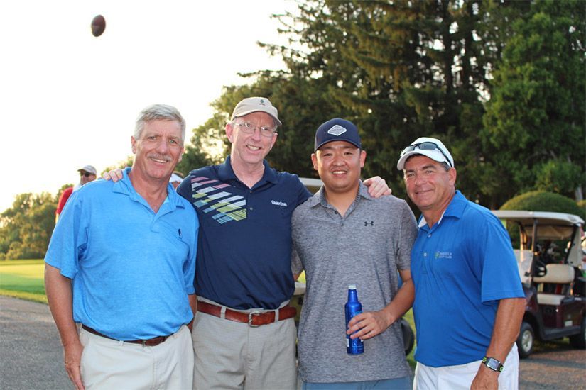Four men are posing for a picture in front of a golf cart
