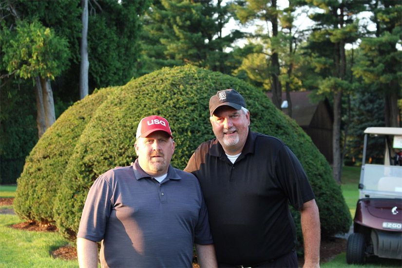 Two men are posing for a picture in front of a golf cart