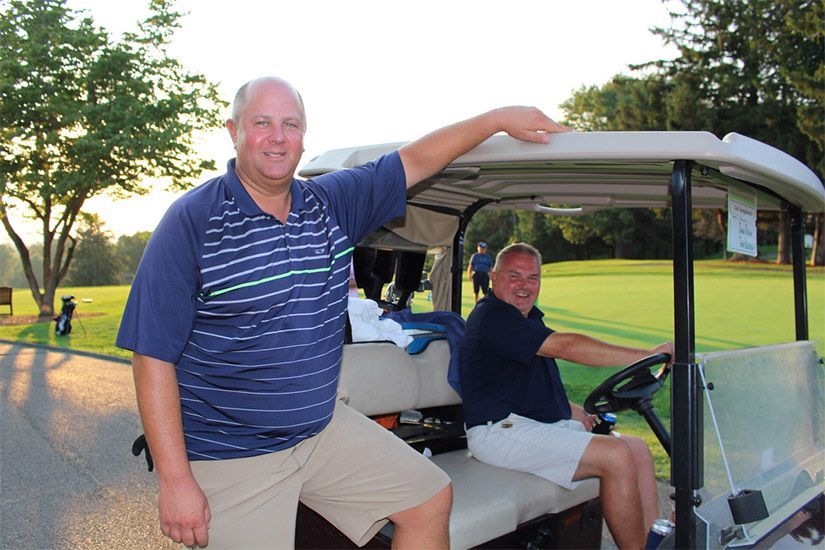 Two men are sitting in a golf cart on a golf course.